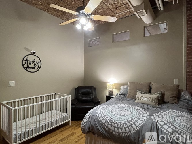 A baby's room with a crib, a chair, a bed, and a ceiling fan.