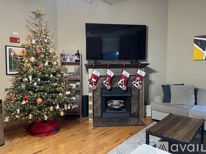 A Christmas tree with a star on top is in a living room with a fireplace and stockings hanging on it.