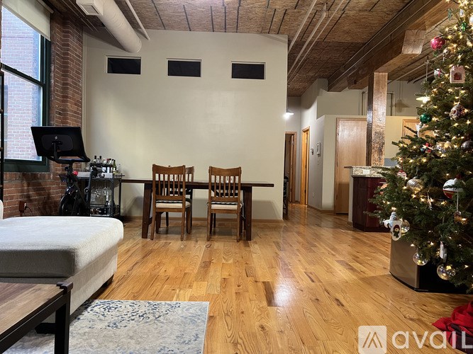 A Christmas tree is in a corner of a room with a bed, a table and chairs.