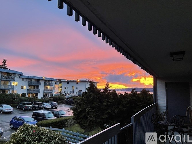 A sunset view from a balcony overlooking a parking lot and buildings.