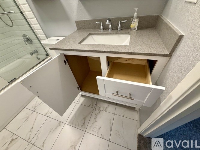 A bathroom with a sink, a shower, and a cabinet under the sink.