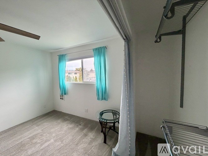 A room with a ceiling fan, a chair, and a window with blue curtains.