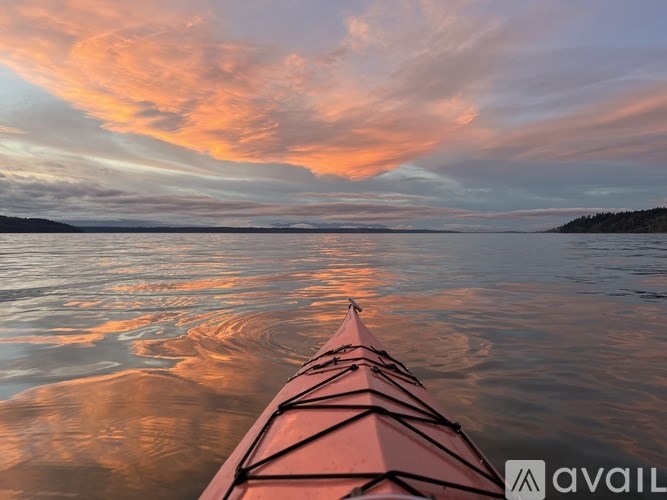 A red kayak is on calm water with a colorful sky in the background.