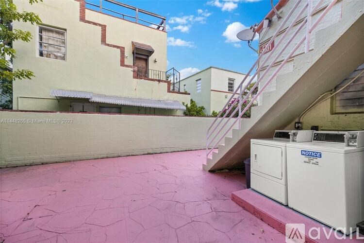 A pink patio area with a white notice board and a staircase leading to a building.