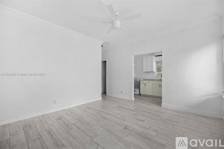 A spacious room with a fan and a kitchen in the background.