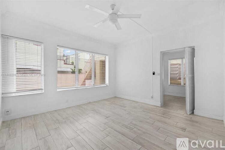 A room with a ceiling fan, wooden flooring, and a window with blinds.
