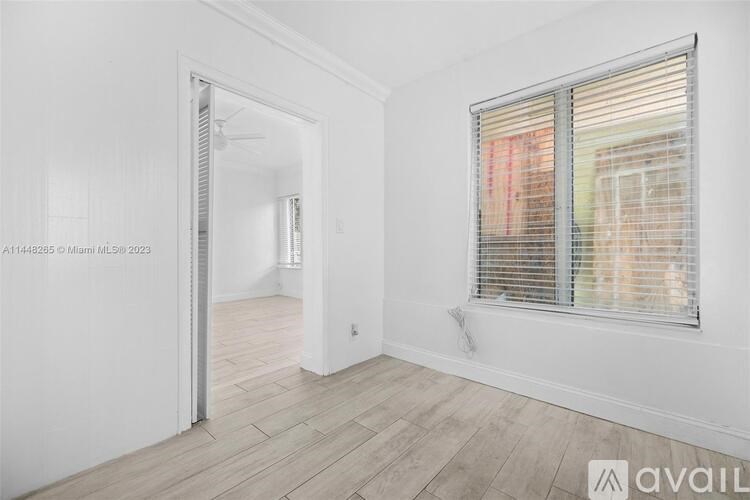 A room with a doorway leading to another room and a window with blinds.