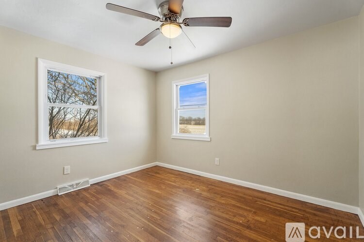 A room with a ceiling fan and two windows.