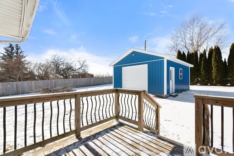 A blue building with a white door is surrounded by a wooden deck and snow.
