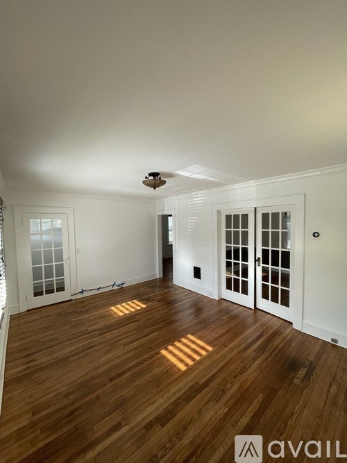 A room with wooden floors and white walls, with a window on the left and a door on the right.