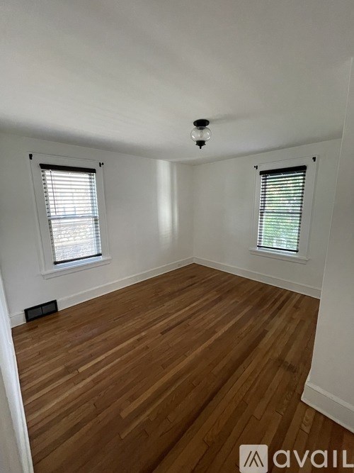 A room with wooden flooring and two windows.