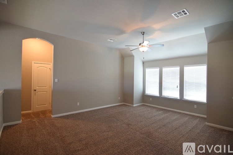 A room with a carpeted floor, a ceiling fan, and a door.