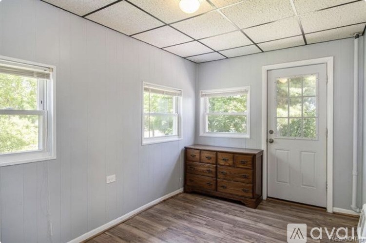 A room with a white door, two windows, and a wooden dresser.
