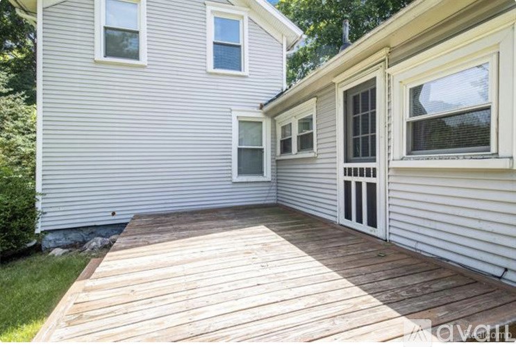 A wooden deck is attached to a house with a white siding.