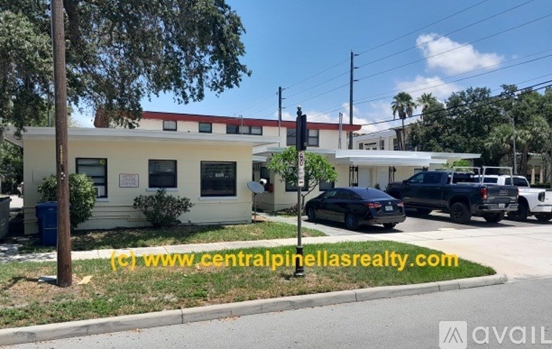 A white building with a red roof is seen with a car parked in front of it.