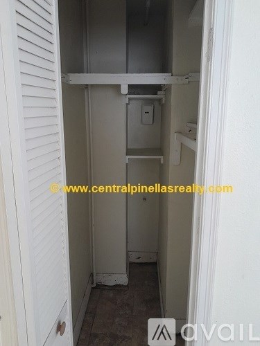 A small, white, metal closet with a shelf and a door.