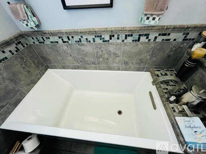 A white bathtub is in a bathroom with a tiled wall.
