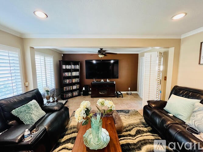 A living room with a black leather couch, a wooden coffee table, and a flat screen TV mounted on the wall.