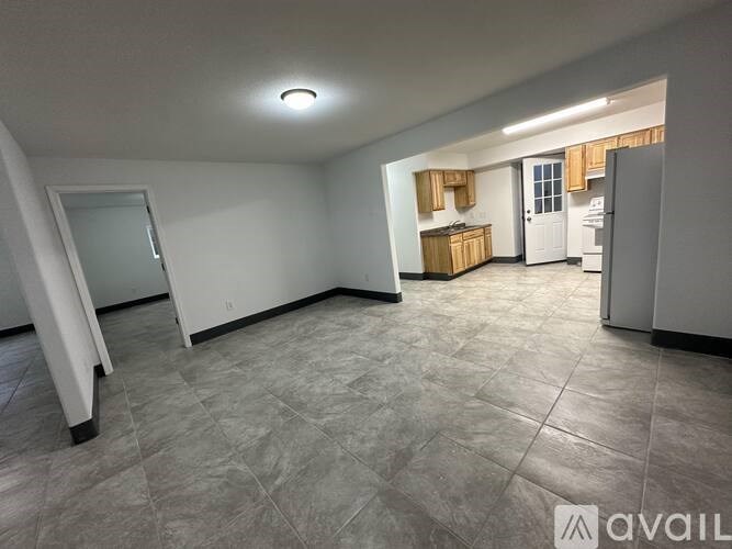 A spacious room with a tiled floor and a kitchen area in the background.