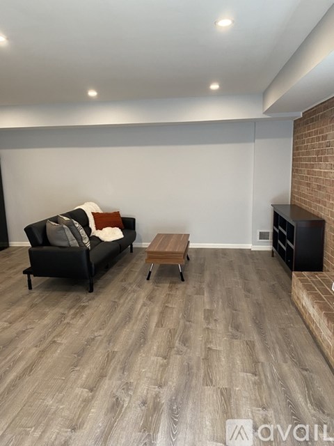 A living room with a black couch, a wooden coffee table, and a brick wall.