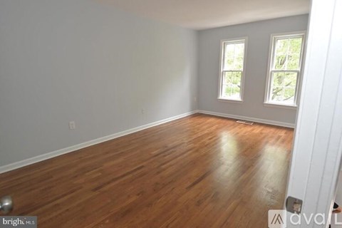 A room with wooden flooring and two windows.