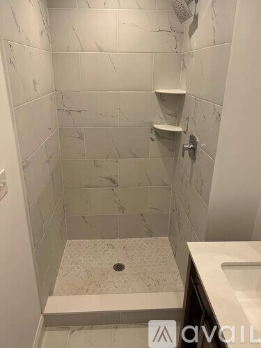A white marble tiled shower with a drain in the middle of the floor.