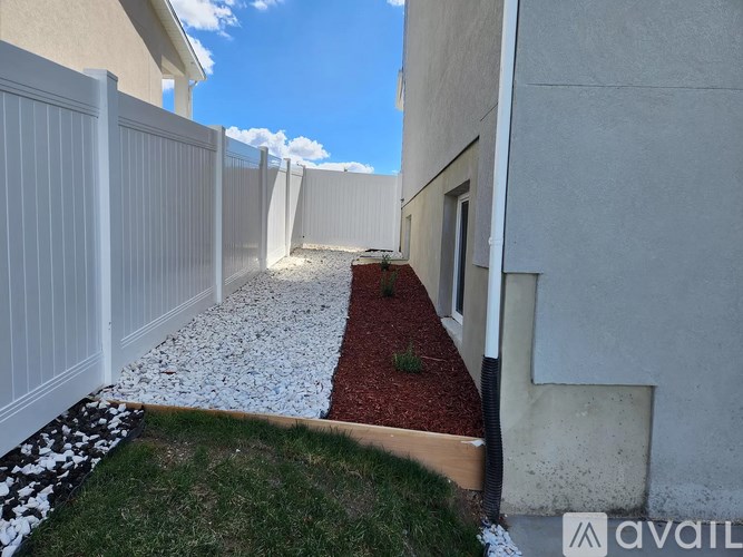 A white fence and a red mulch garden bed are in front of a house.