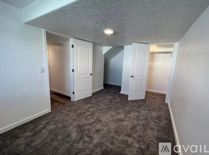 A carpeted room with a white ceiling and walls, and a door on the left.