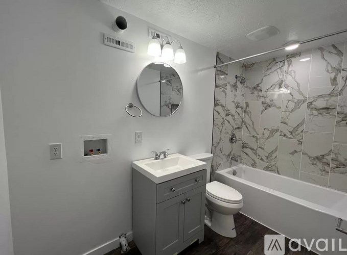 A bathroom with a marble tile shower and a round mirror above a sink.