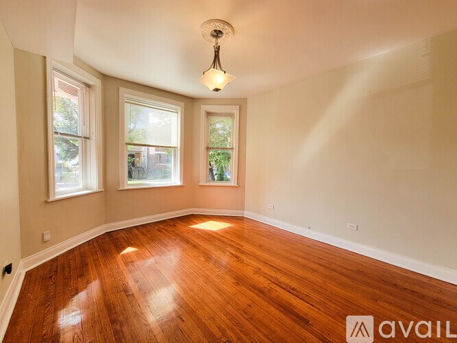A room with wooden floors and a window overlooking a tree-filled street.