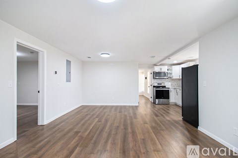 A spacious living room with hardwood floors and a kitchen in the background.