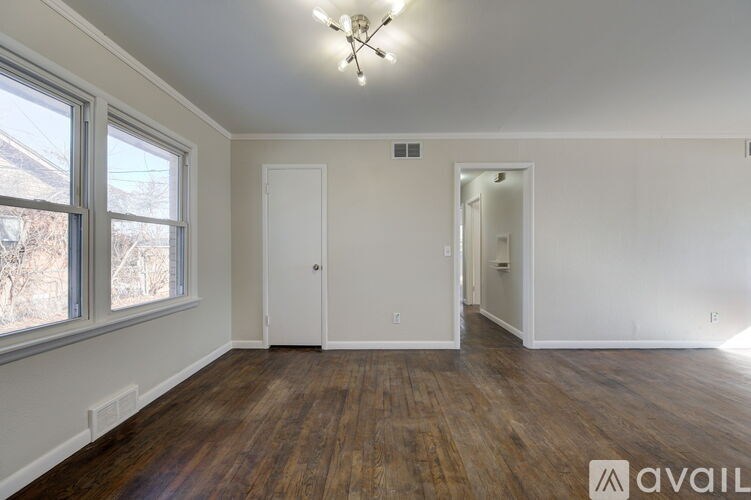 A room with wooden floors and white walls, with a chandelier and two doors.