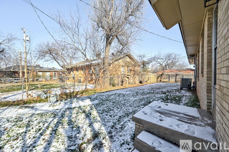 A house with a snow-covered lawn and bare trees in the background.