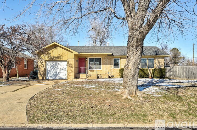 A yellow house with a red door is surrounded by bare trees and a wooden fence.