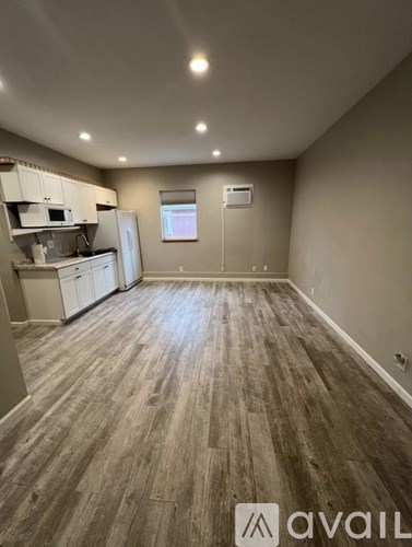 A room with wooden flooring and a kitchen area with white appliances.
