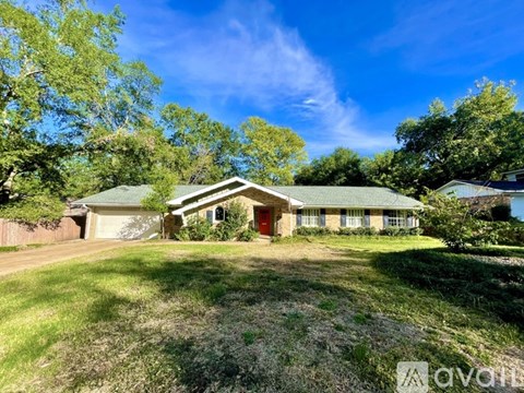 A house with a green roof and a red door is surrounded by trees.
