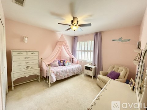 A bedroom with a canopy bed, a dresser, a chair, and a ceiling fan.