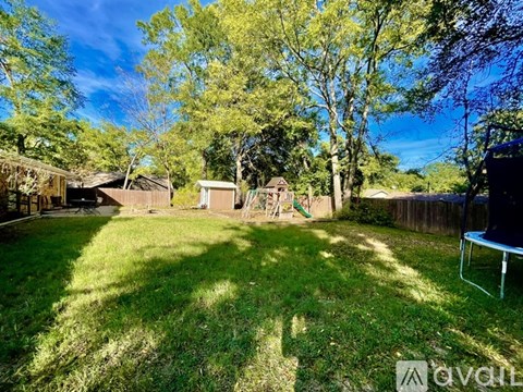 A backyard with a lawn, trees, and a swing set.