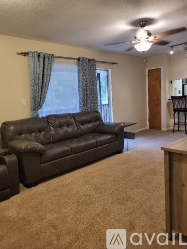 A living room with a black leather couch and a ceiling fan.