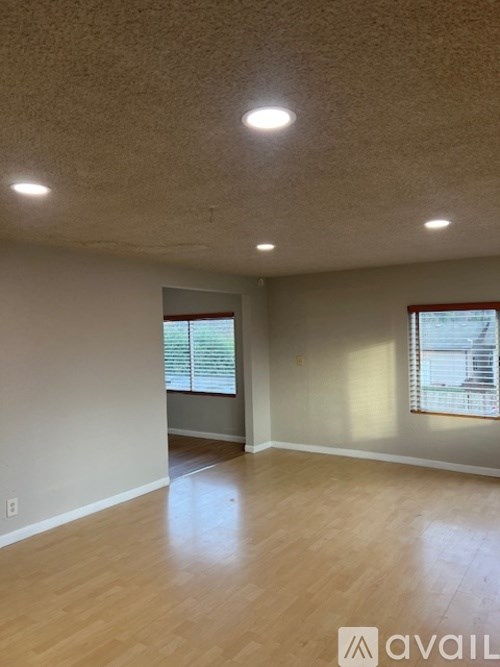 A room with wooden flooring and two windows with blinds.