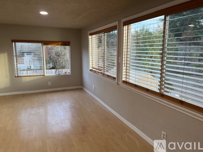 A room with wooden floors and two windows covered with blinds.