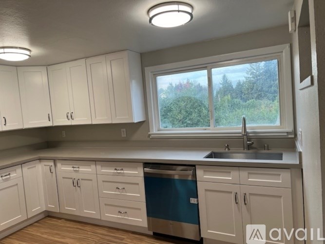 A kitchen with white cabinets and a window overlooking trees.
