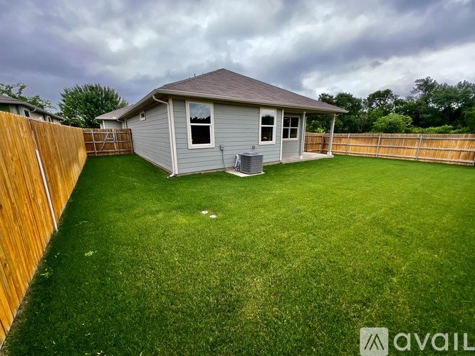 A backyard with a house, fence, and lawn.