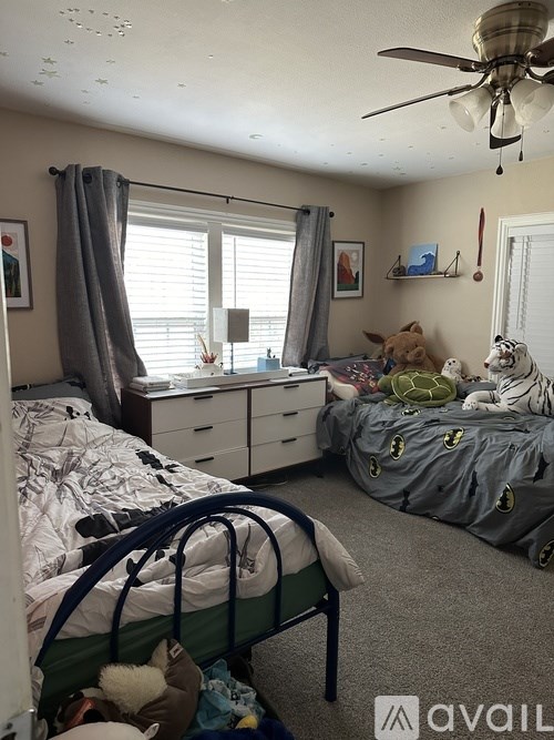 A bedroom with two beds, one of which is made up with a grey comforter and pillows.