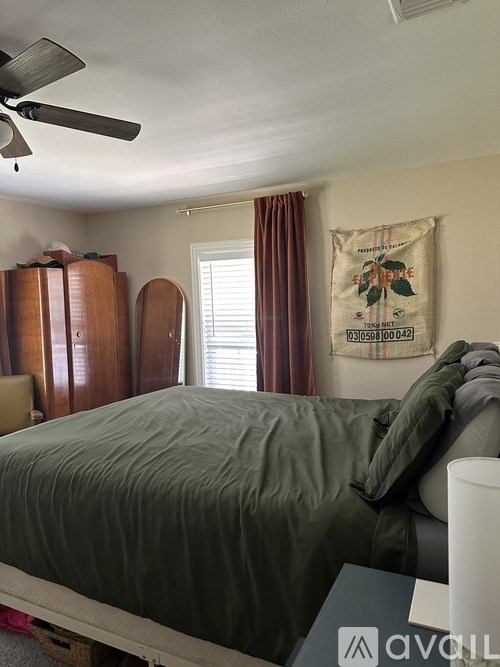 A bedroom with a bed, a fan, and a window with curtains.