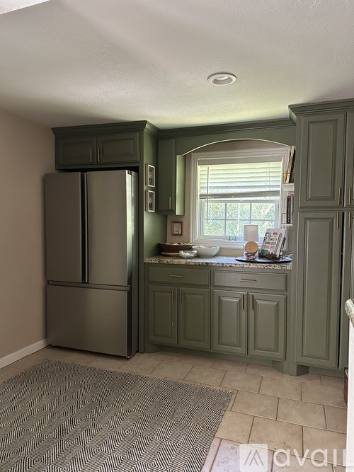 A kitchen with a refrigerator, cabinets, and a window.