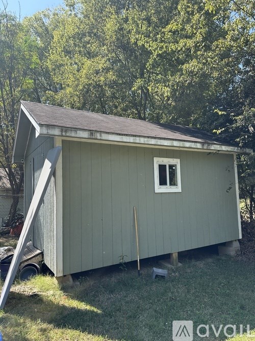 A small grey shed with a brown roof and a single window.