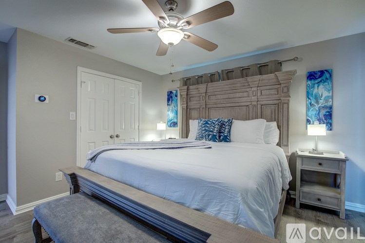 A bedroom with a large bed, a ceiling fan, and a nightstand with a lamp.
