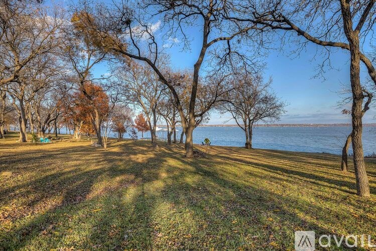A park with trees and a body of water in the distance.