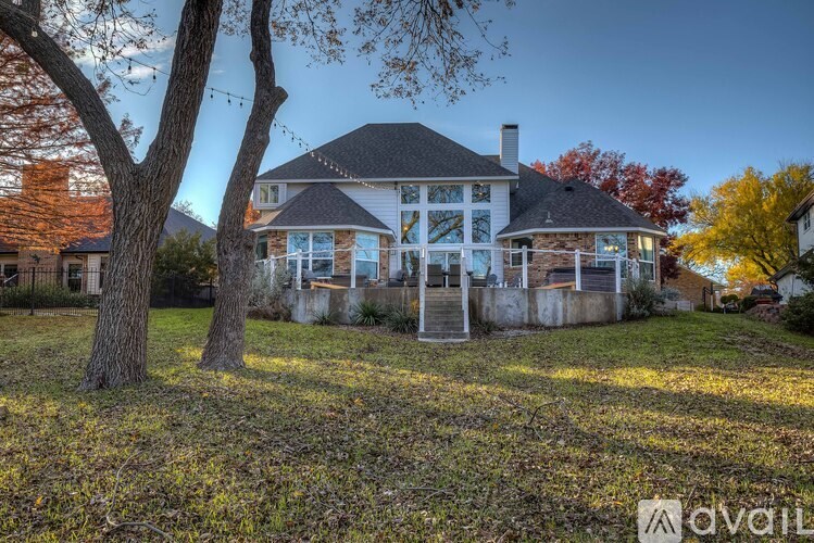 A house with a white exterior and a black roof is surrounded by trees with yellow leaves.